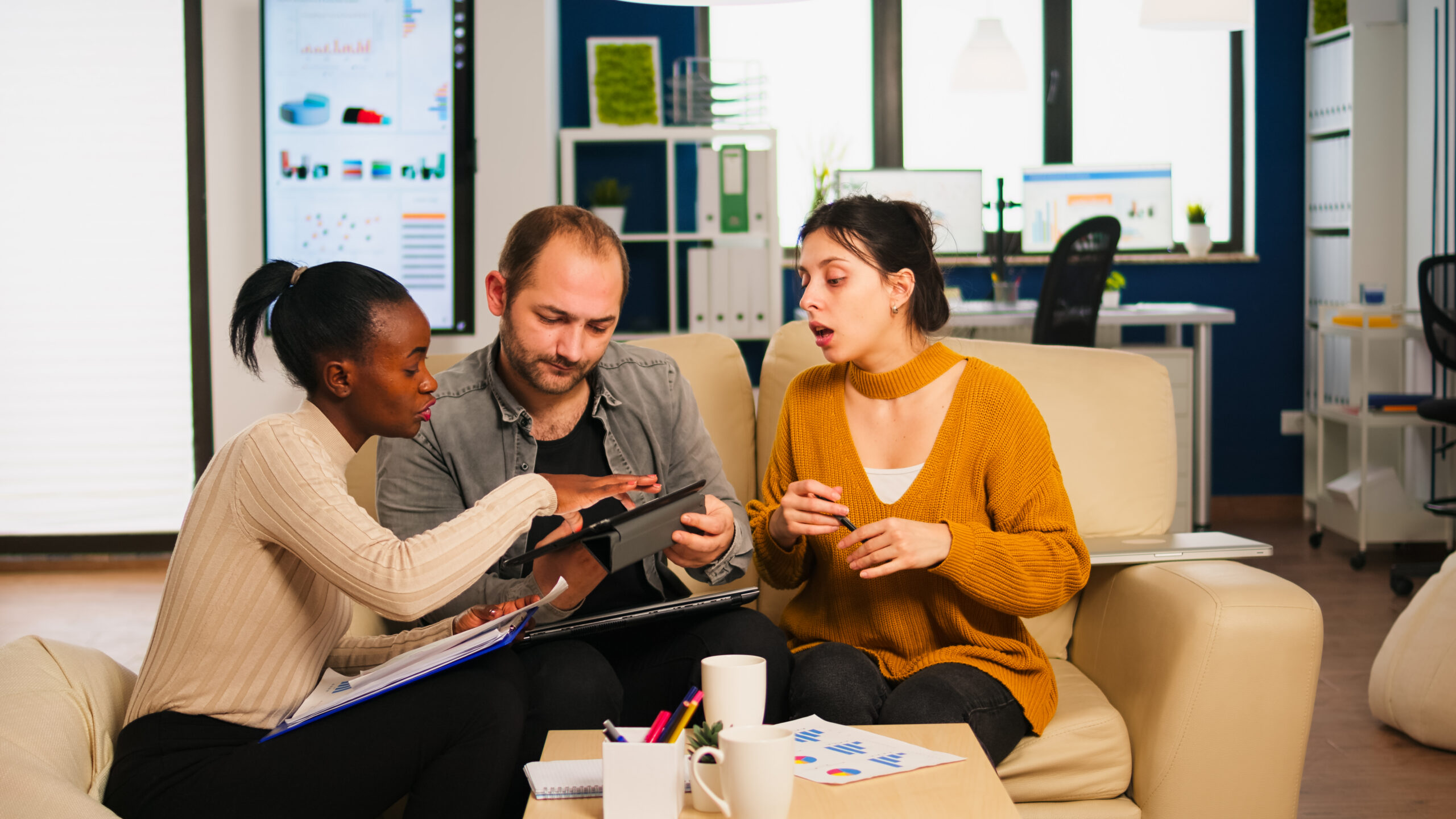 Three entrepreneurs reviewing business plans and financial data on a tablet in an office.